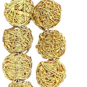 May include: Close-up of a gold necklace with multiple spherical, woven wire beads. The beads are strung together, creating a textured and intricate design. The necklace has a bright, metallic finish.