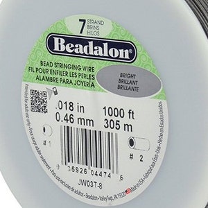 May include: A spool of 7-strand beadalon bead stringing wire. The spool is white with a green label that reads "Beadalon" and includes the text "Bead Stringing Wire", "Fil Pour Enfiler Les Perles", "Alambre Para Joyeria", "Bright", "Brilliant", "Brillante", ".018 in", "0.46 mm", "1000 ft", "305 m", and "JW03T-8".