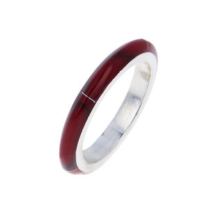 May include: A thin silver band ring with a red enamel inlay. The enamel has a marbled pattern.