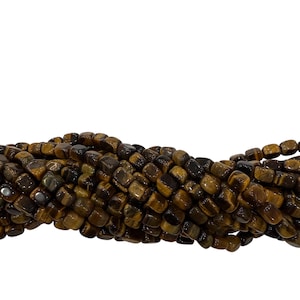 May include: Strand of tiger eye gemstone beads. The beads are a mix of brown and gold tones, with a polished, square shape. The beads are strung together, creating a textured and natural look.