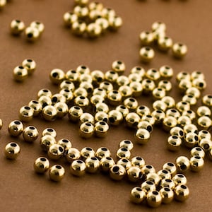 May include: A large quantity of gold-colored round beads. The beads are scattered on a brown surface.