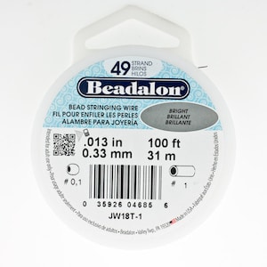 May include: A white spool of Beadalon 49 strand bead stringing wire. The spool is labeled with the text "Beadalon", "Bead Stringing Wire", "Fil Pour Enfiler Les Perles", "Alambre Para Joyeria", "Bright", "Brilliant", "Brillante", ".013 in", "0.33 mm", "100 ft", "31 m", "# 0,1", "# 1", "35926 04685 6", "JW18T-1", "Made in USA - Fabriqué aux États-Unis - Hecho en Estados Unidos".