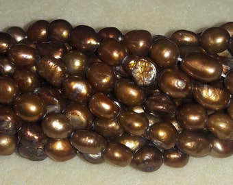 May include: Close-up of a strand of lustrous, bronze-colored freshwater pearls. The pearls have an irregular, oval shape and a smooth, reflective surface. The pearls are strung together, creating a beautiful jewelry piece.