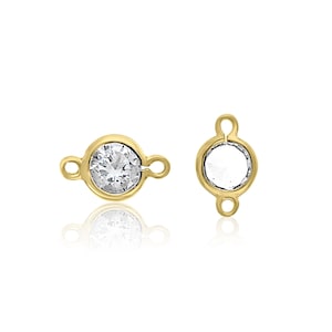 May include: Two gold-tone metal connector charms with a clear round crystal in the center. One charm has a crystal and the other charm is empty.