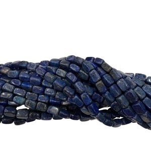 May include: A strand of dark blue lapis lazuli beads. The beads are rectangular with rounded edges, and have a slightly polished appearance. The color varies from deep indigo to lighter shades of blue, with some flecks of gold visible.