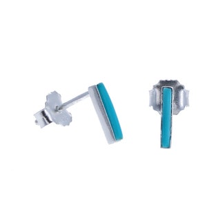 May include: A pair of silver stud earrings with turquoise blue rectangular stones.