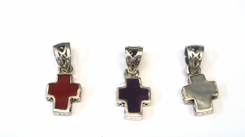 K&ouml;nnte beinhalten: Drei silberne Kreuzanh&auml;nger mit verschiedenen farbigen Einlagen. Das Kreuz links hat eine rote Einlage, das mittlere Kreuz eine violette Einlage und das Kreuz rechts eine wei&szlig;e Einlage.