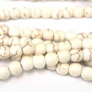 May include: A strand of white howlite beads with brown veining. The beads are round and smooth.