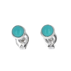 May include: A pair of stud earrings featuring round, turquoise-colored stones set in a silver-colored metal. The earrings have a post and backing for secure wear. The turquoise stones are a vibrant, eye-catching color.