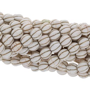 May include: White oval beads with brown stripes. The beads are strung together and are approximately 10mm in diameter.
