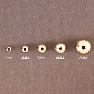 May include: A set of five gold-colored metal beads in different sizes, ranging from 3mm to 8mm. The beads are smooth and have a slightly textured surface.