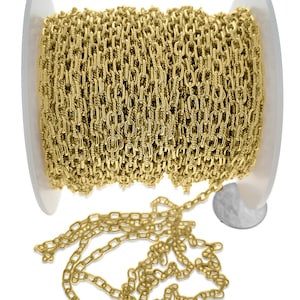 May include: A spool of gold-colored chain with a textured, rectangular link design. The chain is partially unraveled, with a portion of the chain lying loose. The spool is white and the background is white.