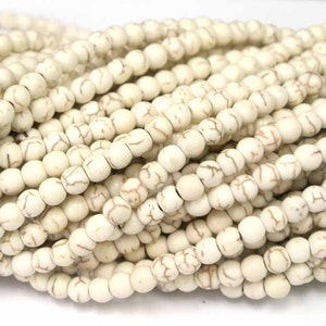 May include: A strand of white howlite beads with brown veining. The beads are round and smooth, and they are strung on a white cord.