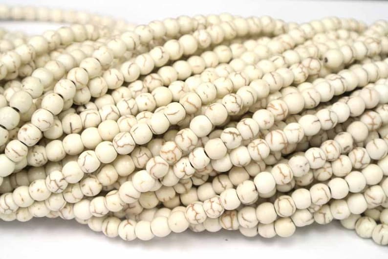 May include: A strand of white howlite beads with brown veining. The beads are round and smooth, and they are strung on a white cord.