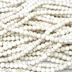 May include: A close-up of a pile of white howlite beads. The beads are round and have a smooth, polished finish. They are ideal for making jewellery or other crafts.