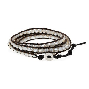 May include: A white pearl wrap bracelet with a brown leather cord and a silver button closure.