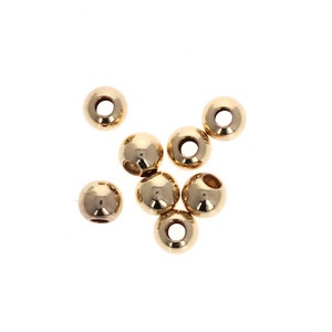 May include: A group of eight gold-colored metal beads with a hole in the center of each bead.
