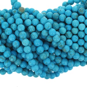May include: Close-up of a strand of turquoise beads. The beads are round, with a light blue color and brown marbling. The beads are strung together, creating a textured surface. Ideal for jewelry making.