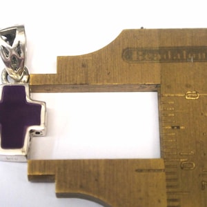 K&ouml;nnte beinhalten: Ein silberner Kreuzanh&auml;nger mit einem violetten Emaille-Zentrum. Der Anh&auml;nger ist etwa 2,5 cm gro&szlig;.