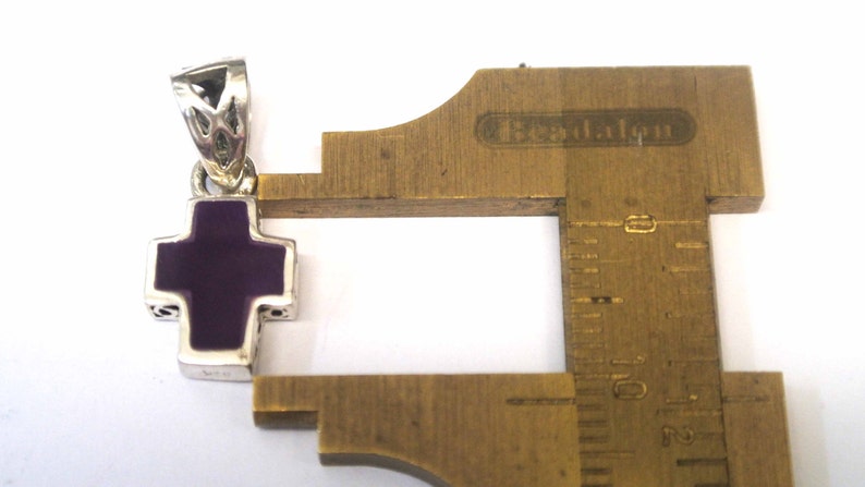 K&ouml;nnte beinhalten: Ein silberner Kreuzanh&auml;nger mit einem violetten Emaille-Zentrum. Der Anh&auml;nger ist etwa 2,5 cm gro&szlig;.