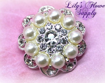 May include: A silver flower-shaped embellishment with a central rhinestone surrounded by white pearls.