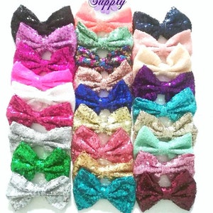 May include: A collection of 18 sequined bows in various colors, including pink, green, blue, gold, and silver. The bows are arranged in rows and are all the same size.  Lily's Flower Supply is printed at the top of the image.