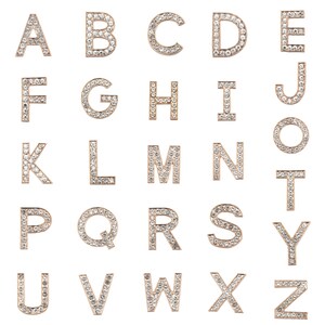 Puede incluir: Un conjunto de abalorios de letras del alfabeto de color dorado, cada letra est&aacute; incrustada con diamantes de imitaci&oacute;n transparentes. Las letras est&aacute;n dispuestas en orden alfab&eacute;tico.