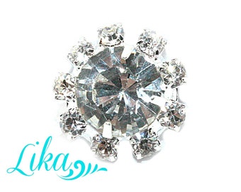 May include: A silver-toned rhinestone embellishment with a large, clear, faceted crystal in the center surrounded by smaller rhinestones.