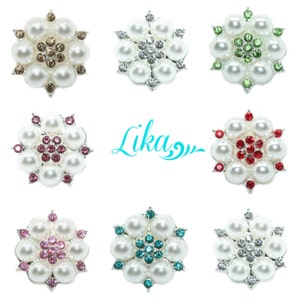 Puede incluir: Nueve adornos de perlas y diamantes de imitación en varios colores, incluidos blanco, marrón, verde, rojo, rosa y azul. Cada adorno presenta un grupo central de diamantes de imitación rodeado por un anillo de perlas.