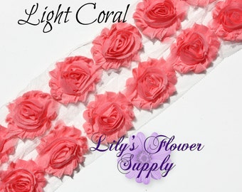 May include: Light coral fabric flower trim with a white mesh backing. The trim features a row of fabric flowers with a ruffled design.