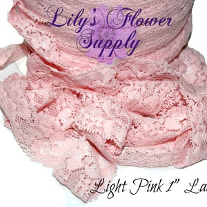 May include: Light pink lace ribbon, 1 inch wide, is displayed in a rolled form. The delicate fabric is intricately patterned with floral designs. The text "Lily's Flower Supply" is visible in the image.