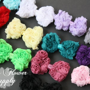 Peut inclure: Une collection de nœuds de cheveux en tissu fleuri faits à la main dans différentes couleurs, notamment turquoise, rose, violet, vert et crème. Les nœuds sont disposés en rangée sur une surface grise.  Lily's Flower Supply.