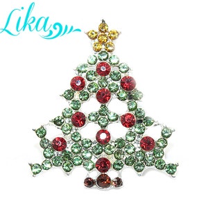 May include: A silver Christmas tree brooch with red and green rhinestones. The tree is decorated with a yellow star on top.
