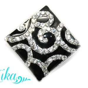 May include: A black and silver square brooch with a swirling design and clear rhinestones.