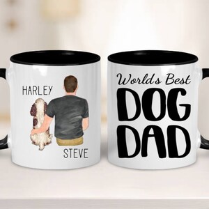 May include: White ceramic mug with a black rim and handle. One side features a cartoon illustration of a person holding a dog with the text "Harley" and "Steve". The other side features the text "World's Best Dog Dad".