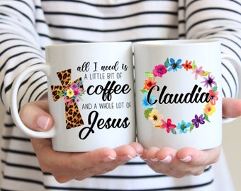 Könnte beinhalten: Zwei weiße Keramikbecher mit schwarzem Text und bunten Blumenmustern. Ein Becher sagt "alles was ich brauche ist ein bisschen Kaffee und eine ganze Menge Jesus" mit einem Leopardenmusterkreuz und Blumen. Der andere Becher sagt "Claudia" mit einem Blumenkranz.