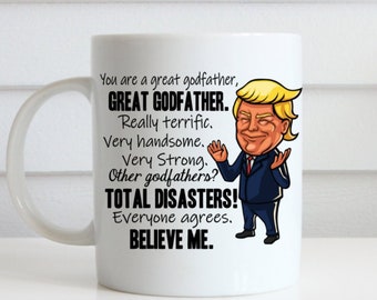 Puede incluir: Taza de cerámica blanca con una imagen de dibujos animados de un hombre con cabello rubio que lleva un traje azul y una corbata roja. La taza tiene texto que dice "You are a great godfather, GREAT GODFATHER. Really terrific. Very handsome. Very Strong. Other godfathers? TOTAL DISASTERS! Everyone agrees. BELIEVE ME."