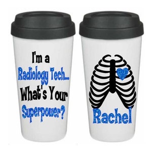 May include: Two white travel mugs with black lids. One mug has the text "I'm a Radiology Tech... What's Your Superpower?" The other mug has a black outline of a ribcage with a blue glitter heart and the name "Rachel" in blue glitter.