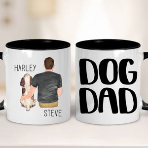 May include: Two white ceramic mugs with black rims. One mug features a cartoon illustration of a person with a dog, with the text "Harley" and "Steve". The other mug has the text "DOG DAD" in black.
