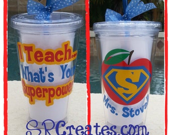 Puede incluir: Dos vasos de plástico transparentes con pajitas y lazos de lunares azules y blancos. Un vaso tiene el texto "I Teach... What's Your Superpower" en amarillo, rojo y azul. El otro vaso tiene una manzana roja con un logotipo de Superman azul y el texto "Mrs. Stova" en azul. Ambos vasos están sobre una superficie blanca.