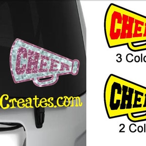 May include: A white, silver, and pink glitter cheer megaphone decal with the word "CHEER" in pink. The decal is on a black car with the website "SRCreates.com" in yellow text. There are two other megaphone decals, one with yellow and red text and one with yellow and black text.