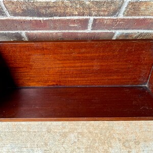 May include: A dark brown wooden shelf with a curved front edge. The shelf is empty and appears to be made of solid wood.