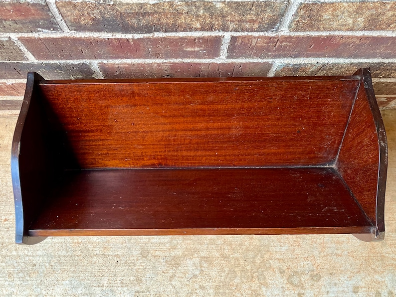 May include: A dark brown wooden shelf with a curved front edge. The shelf is empty and appears to be made of solid wood.