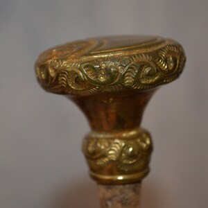 May include: A gold-colored metal walking stick handle with intricate floral designs.