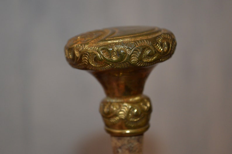 May include: A gold-colored metal walking stick handle with intricate floral designs.