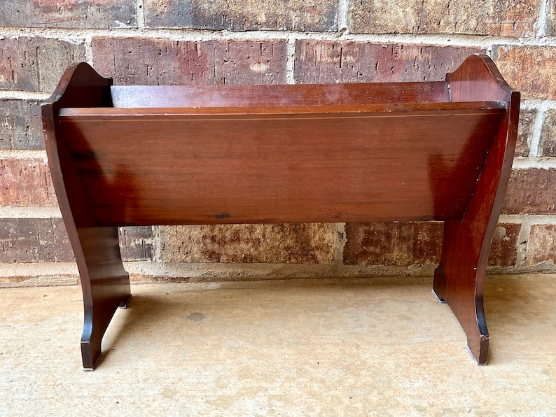 May include: A wooden doll cradle with a dark brown finish. The cradle has a rectangular shape with rounded edges and stands on four legs.