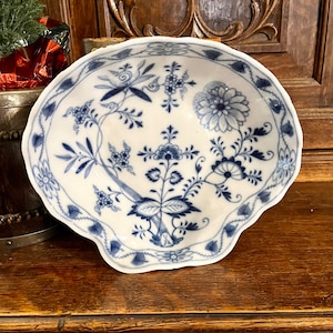 May include: A white porcelain bowl with a scalloped edge and a blue and white floral pattern. The bowl is decorated with a delicate floral design, including a large blue flower in the center.