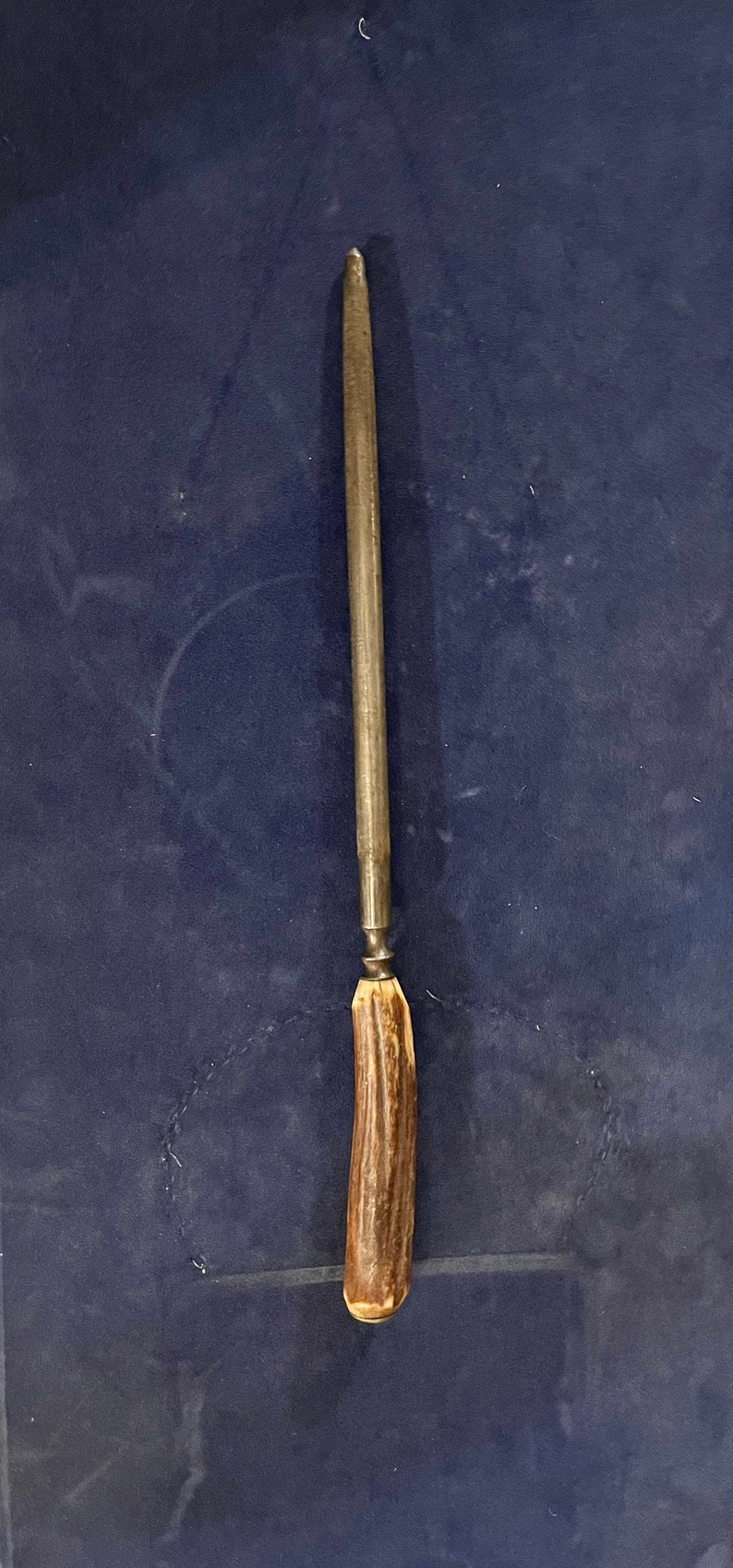 May include: A long, thin, metal knife sharpener with a brown antler handle.