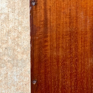 May include: Close-up of a dark brown wooden surface with a lighter wood border. The wood has a natural grain pattern and there are two small nails visible in the border.
