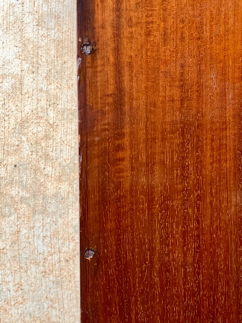 May include: Close-up of a dark brown wooden surface with a lighter wood border. The wood has a natural grain pattern and there are two small nails visible in the border.